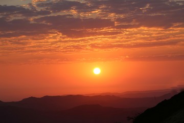 Landscape view of the sunrise from top to the mountain with orange color shade in the background with sun