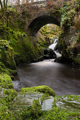 bridge in the scotish woods with flowing cascade of water