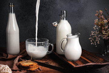 Still life in rustic style. Milk in a glass bowl and cookies. Milk pours into a mug