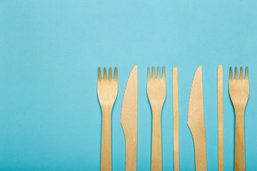 Wooden forks and knives for food in a paper cup on a colored background. Eco-friendly disposable tableware without plastic
