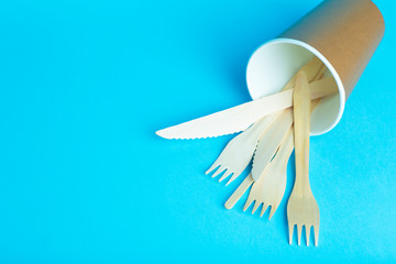 Wooden forks, knives and spoons for food in a paper cup on a colored background. Eco-friendly disposable tableware without plastic