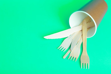 Wooden forks, knives and spoons for food in a paper cup on a colored background. Eco-friendly disposable tableware without plastic