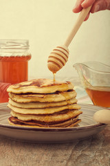 A large stack of steaming pancakes on a white plate with syrup being poured and dripping down the sides on a golden brown background