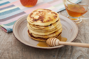 A large stack of steaming pancakes on a white plate with syrup being poured and dripping down the sides on a golden brown background