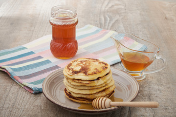 A large stack of steaming pancakes on a white plate with syrup being poured and dripping down the sides on a golden brown background