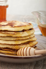 A large stack of steaming pancakes on a white plate with syrup being poured and dripping down the sides on a golden brown background