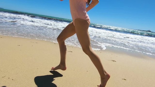 Little girl wearing pink swimsuit running on the beach barefoot. Slow motion