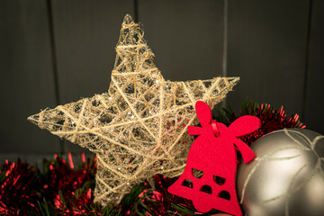 Christmas decoration with golden star, red velvet bell and silver ball on red and green tinsel with dark wood background