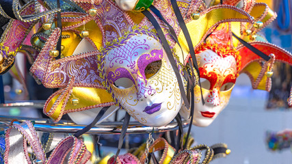 Showcases with beautiful Venetian masks with plumage for carnival, different goods, clothes, scarfs. Shopping 