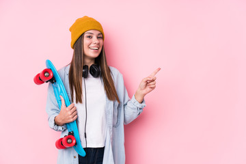 Young skater woman holding a skate smiling and pointing aside, showing something at blank space. © Asier