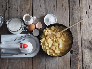 On the kitchen cutting board baking dish with dough. Ingredients and kitchen utensils nearby on an ancient wooden table.