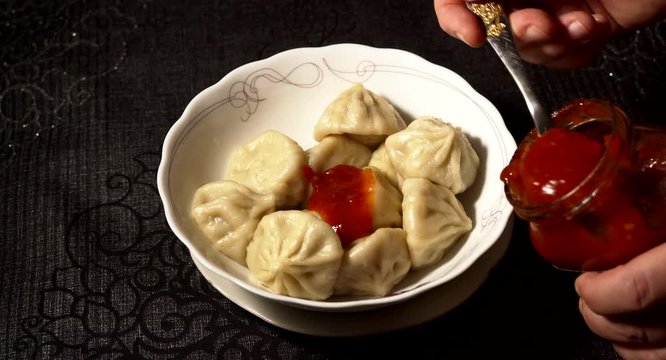 Close up of spinning wooden plate of delicious khinkali dumplings seasoned with chili pepper and decorating with fresh parsley