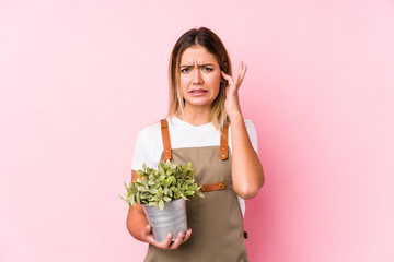 Young caucasian gardener woman in a pink background covering ears with hands.