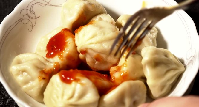 Close up of spinning wooden plate of delicious khinkali dumplings seasoned with chili pepper and decorating with fresh parsley