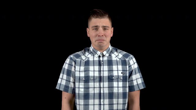 A young man shows an emotion of sadness. Sad man in a shirt on a black background