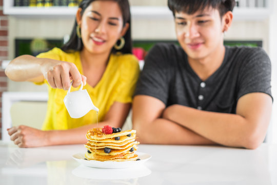 Young Asian man and woman couple sitting at dinner table woman pour sauce onto pancake, focus on pancake.