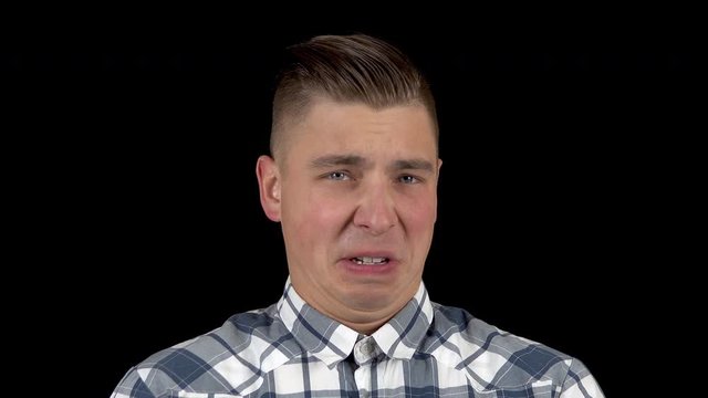The young man shows disgust on his face. Close-up of a man writhing his face in disgust on a black background closeup