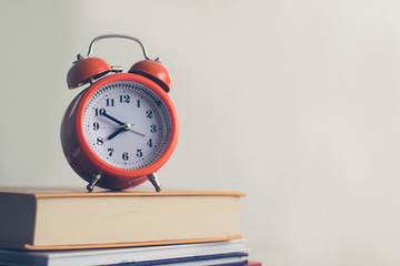Orange old mechanical clock on books background. White background. Defocused books. Learning concept. Time to read books. Old-fashioned. Personality development. Improvement of cognitive functions.
