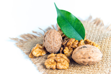 Close up of healthy raw walnuts placed on a rustic woven brown mat, decorated with green leaves, isolated on a white background