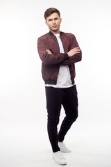 Young european man in white sweater and black pants, red bomber jacket posing on white background....