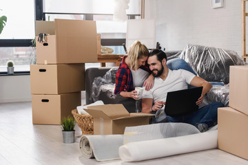 Young couple moving in new home.Sitting on floor and relaxing after unpacking.Looking something on laptop