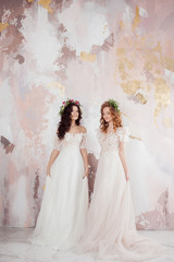 Two charming brides in beautiful spring wreaths on their heads. Beautiful young women in wedding dresses