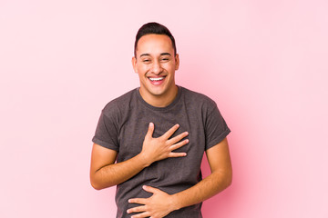 Yooung latin man posing in a pink backgroundlaughs happily and has fun keeping hands on stomach.