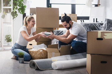 Happy young couple unpacking or packing boxes and moving into a new home  - obrazy, fototapety, plakaty