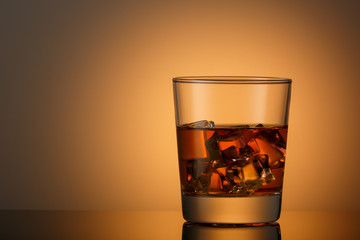 A glass of whiskey with ice on a dark surface with a reflection. Space for text