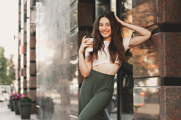 Beautiful smiling woman drink coffee walking on the city in summer day.