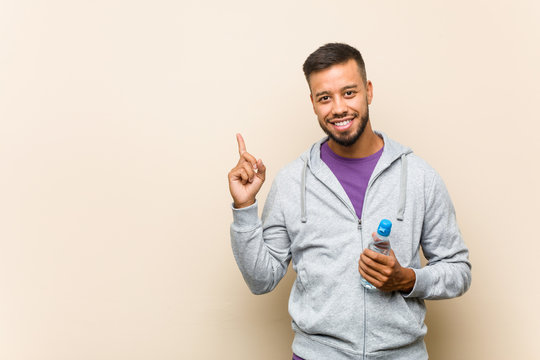 Young mixed race asian man holding a water bottle smiling cheerfully pointing with forefinger away.
