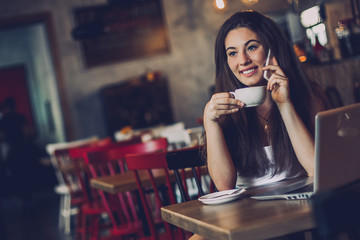 Business woman talking to the phone, working on a laptop and drinking coffee in a cafe.