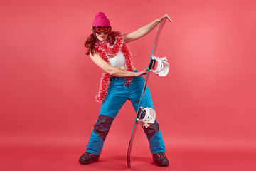 Studio shot woman in rad wearing ski clothes standing with snowboard n a red background with tinsel and ski mask