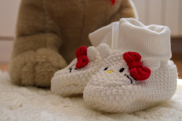 Fototapeta na wymiar Knitted baby shoes for girl with big teddy bear in background