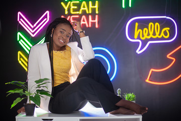 African-American girl sitting on a background of neon signs on a black background. Beautiful young...