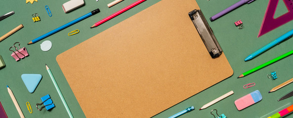 School stationery on green background. The concept banner with student supplies for back to school. Notebook, pens, pencils, and other tools. Empty space for the template.Banner