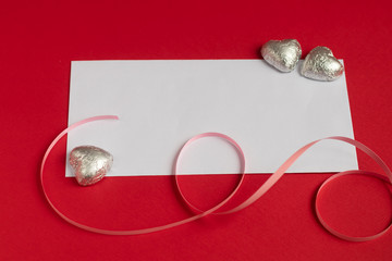 Valentines day concept. On a red background, in the center there is a white rectangle for inscription. Hearts and ribbons.