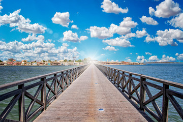 Fototapeta premium Long wooden bridge leading over a sea lagoon. It leads to Fadiouth Island in Senegal, Africa. Sun rays shine from the end of the bridge. It is a beautiful natural background.