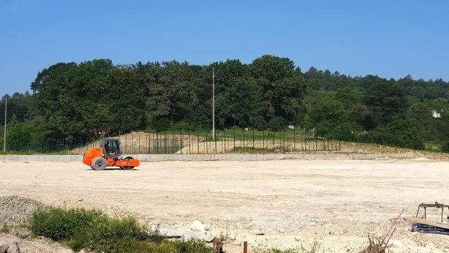 Construction worker is driving huge road roller with spikes and compacting soil for a large foundation.