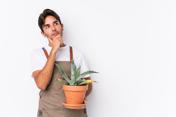 Young caucasian gardener man holding a plant isolated looking sideways with doubtful and skeptical...