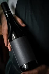 Küchenrückwand glas motiv A full Bottle of wine in the hands of a male sommelier with a black label. Mock-up for red wine design. © Andrey