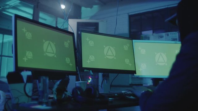 Man in the cap is sitting and working on stealing data at the computer as haker. Hideout Place has Dark Atmosphere.