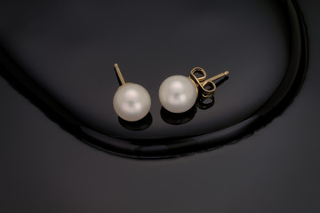 A close up of a pair of white pearl earring studs with yellow gold post and nut on a black...
