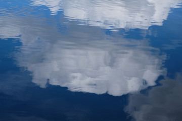 Fototapeta premium Reflection of fluffy clouds on the water surface. Blue and white colors dominates.