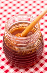 Fototapeta premium Jar of Fresh Raw Organic Honey on a Red and White Table Cloth