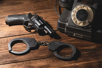 Black pneumatic gun, bracelets and old telephone on the table. Detective agent desk concept.