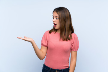 Young brunette girl over isolated blue background holding copyspace imaginary on the palm