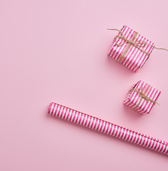 two gifts wrapped in pink striped paper and paper roll on a pink background