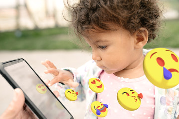 Little Girl playing with a mobile phone touching the screen with her finger, emoticons coming out of the screen