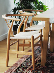 Close view of wooden two chairs near with table in a white dining room interior with oriental carpet. Interior design in minimal style.